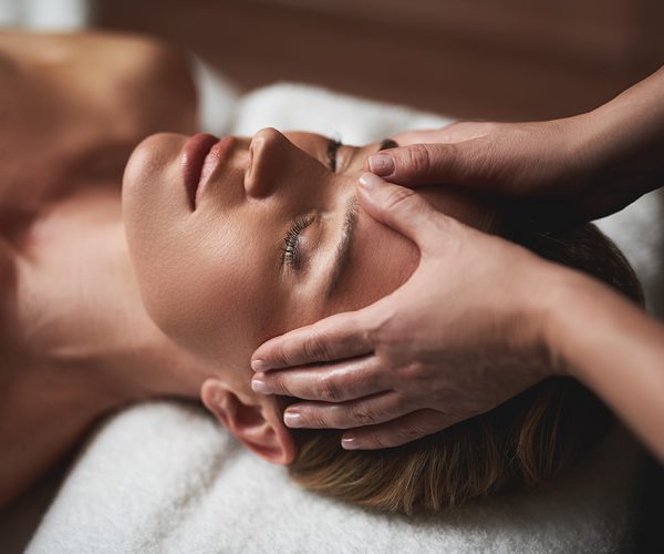 Concept of relaxation and body care. Top angle portrait of female therapist making anti-age massage of forehead wrinkles to young woman in spa salon